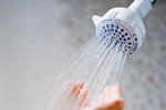Nahaufnahme eines Duschkopfes mit laufendem Wasser, das auf eine Hand trifft. Die Sparbrause hilft, 