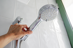 Eine Hand greift nach einem Duschkopf. Dieses Bild steht symbolisch für die Reduktion des Wasserflus
